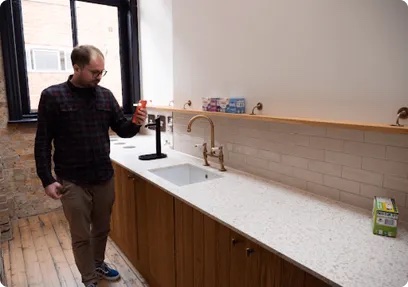 A tester walking towards a kitchen counter holding a phone, far from the pack